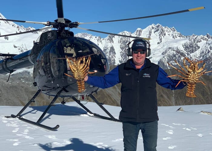 Gus holding crayfish in front of helicopter on snow