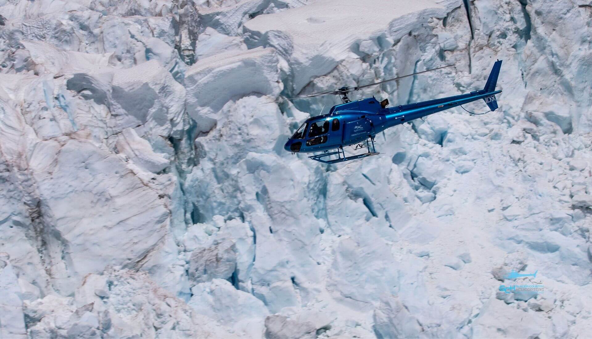 Blue helicopter flying over glacier ice